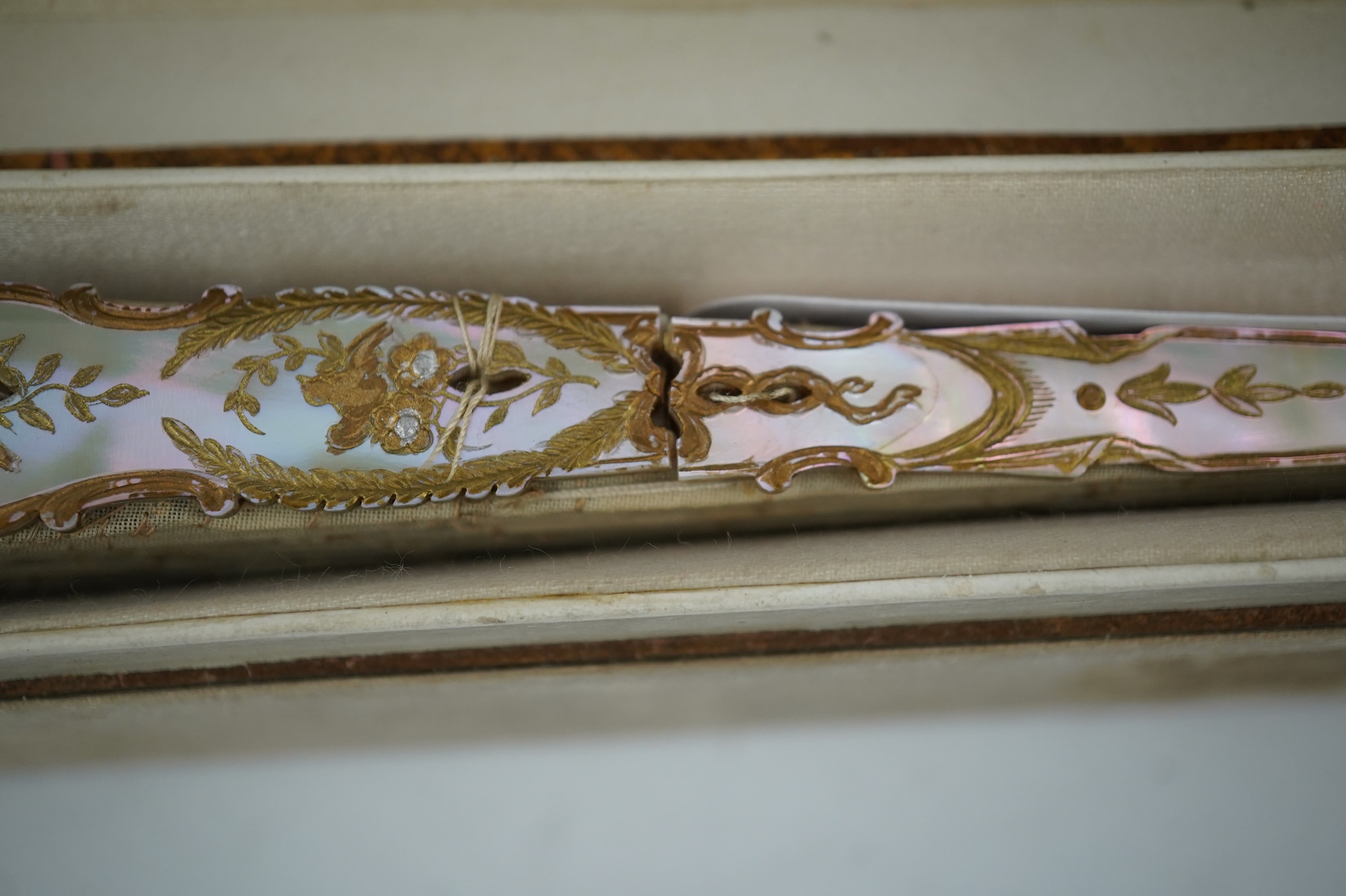 Three French fans: a mother of pearl and sequin fan boxed, a painted silk, feather and bone fan and a gilt decorated bone figural paper fan, the two bone fans having gilt mirrored mounts on the guards, figural paper fan